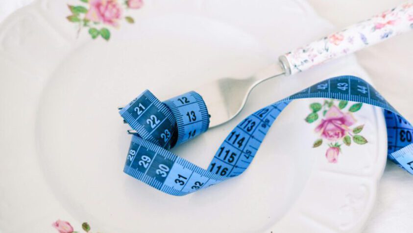 A floral plate with a fork and blue measuring tape symbolizing dieting or healthy eating.